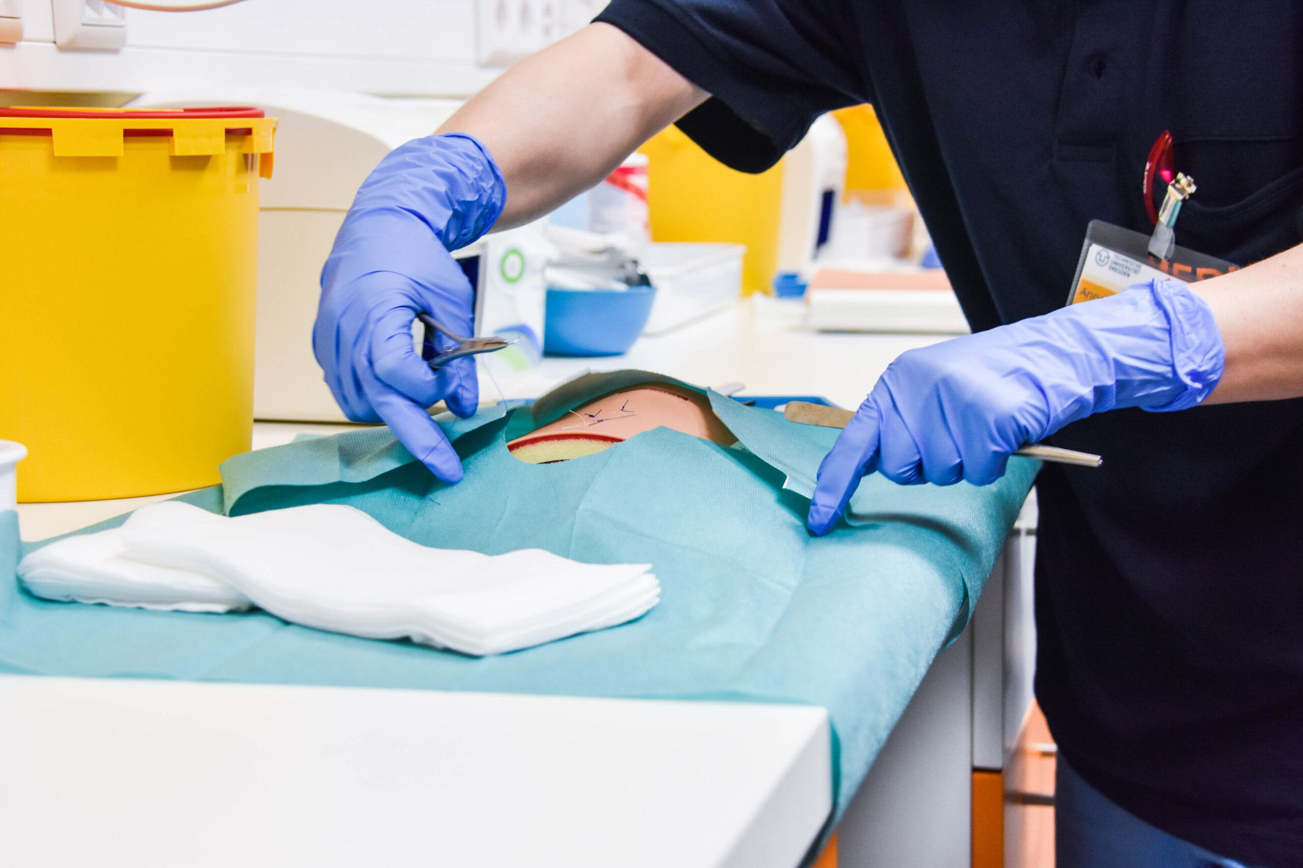 Eine Person in chirurgischen Handschuhen näht eine Wunde auf der künstlichen Haut