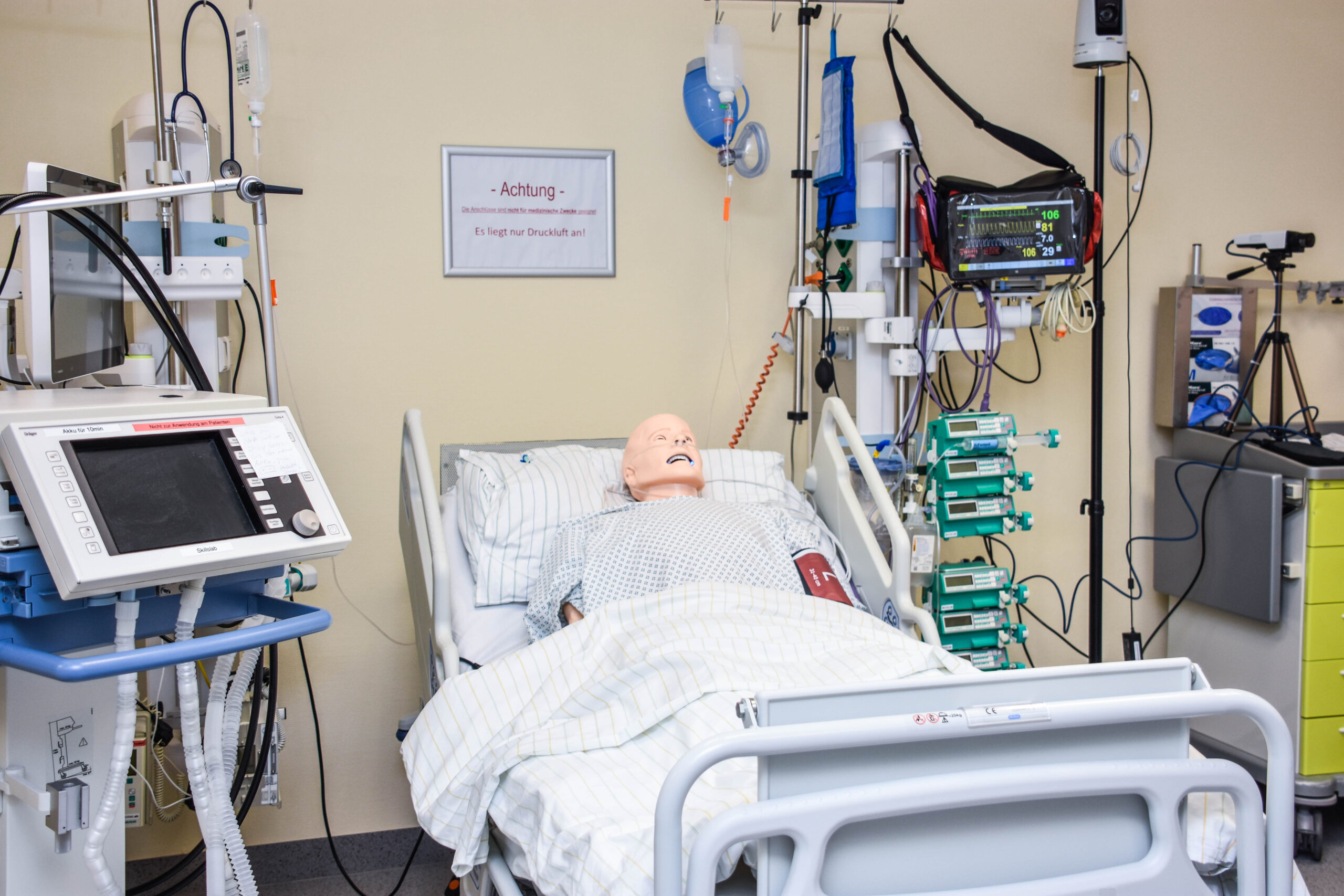 Eine medizinische Puppe eines erwachsenen Menschen liegt verkabelt im Krankenhausbett, umgeben von medizinischen Geräten